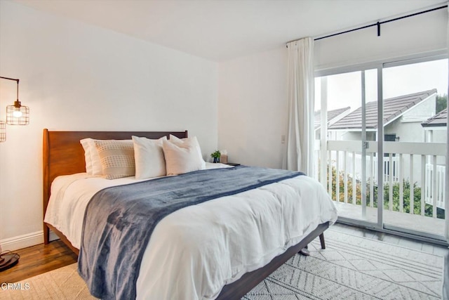 bedroom with baseboards, wood finished floors, and access to exterior