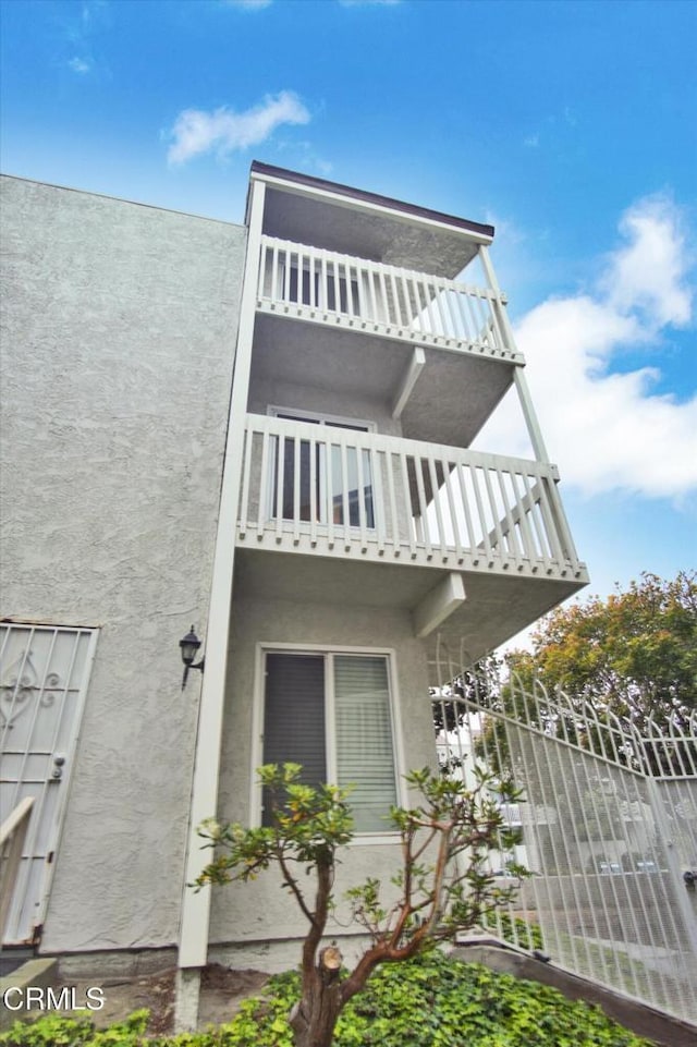 view of home's exterior with stucco siding, a balcony, and fence
