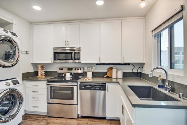 kitchen featuring stacked washer and dryer, a sink, white cabinets, stainless steel appliances, and recessed lighting