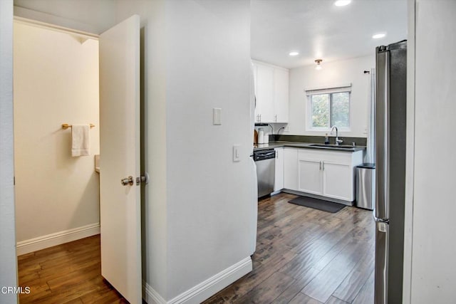 kitchen featuring appliances with stainless steel finishes, a sink, baseboards, white cabinets, and dark wood-style floors