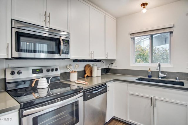 kitchen featuring stainless steel appliances, dark countertops, white cabinetry, and a sink