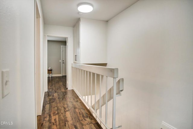 hallway featuring baseboards, an upstairs landing, and dark wood-type flooring