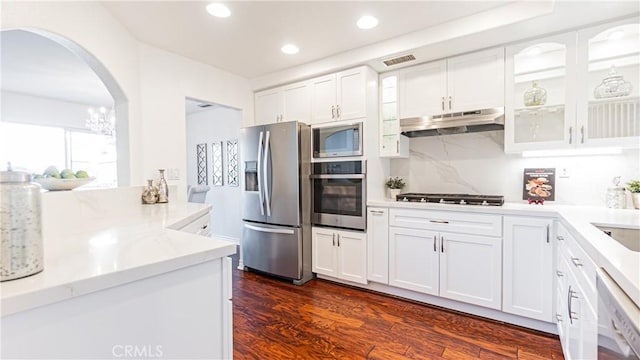 kitchen with appliances with stainless steel finishes, arched walkways, under cabinet range hood, visible vents, and glass insert cabinets