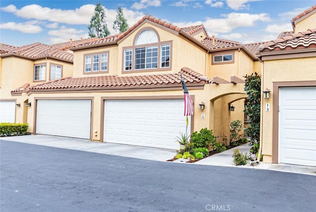 mediterranean / spanish-style home featuring an attached garage, concrete driveway, a tile roof, and stucco siding