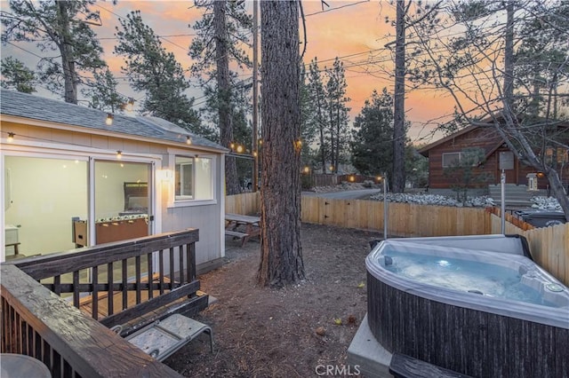 yard at dusk featuring fence, an outdoor structure, and a hot tub