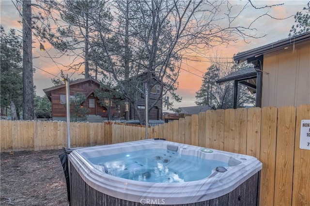 yard at dusk with fence and a hot tub
