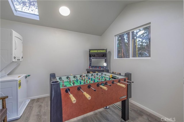 recreation room featuring stacked washer and clothes dryer, vaulted ceiling, wood finished floors, and baseboards