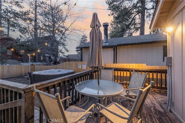 deck at dusk with a jacuzzi, outdoor dining space, and a fenced backyard