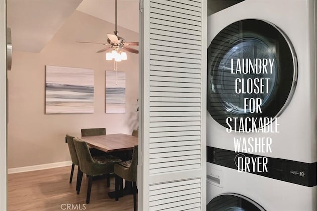 laundry room featuring laundry area, a ceiling fan, baseboards, wood finished floors, and stacked washer and clothes dryer