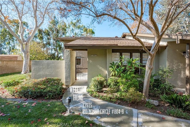 entrance to property with stucco siding, a gate, and fence