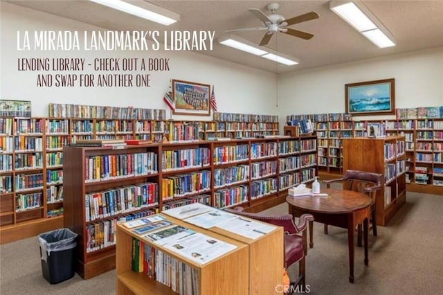 sitting room with a ceiling fan, wall of books, and carpet flooring