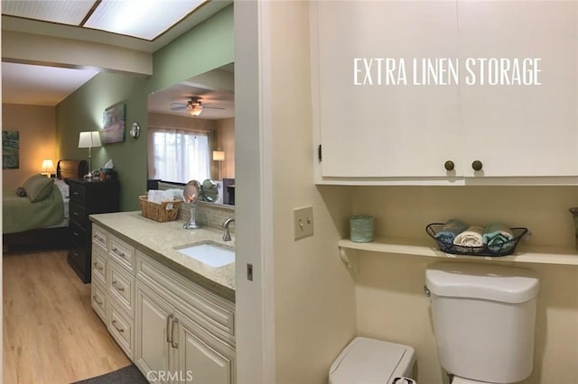 ensuite bathroom featuring ceiling fan, vanity, toilet, wood finished floors, and ensuite bathroom