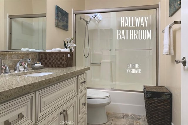 full bathroom with stone finish floor, backsplash, vanity, toilet, and shower / bath combination with glass door