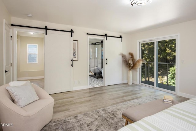 bedroom with wood finished floors, a barn door, access to outside, and baseboards