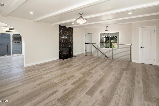 unfurnished living room with an inviting chandelier, light wood-style floors, beamed ceiling, and baseboards
