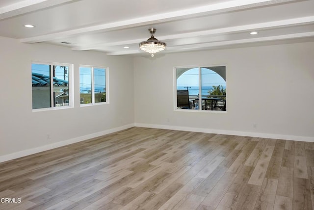 unfurnished room featuring beam ceiling, baseboards, a wealth of natural light, and light wood finished floors