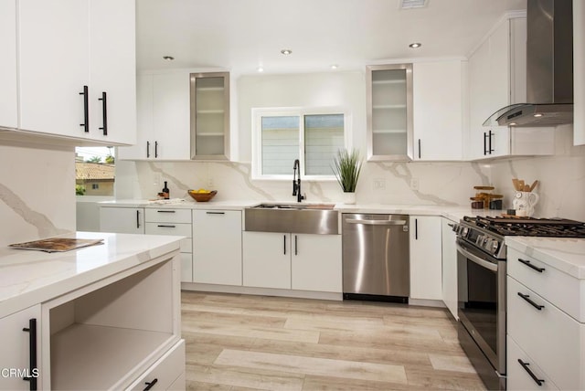 kitchen featuring light stone countertops, stainless steel appliances, wall chimney range hood, and a sink