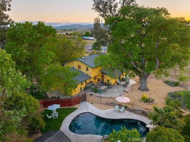 pool at dusk with a patio, fence, and a fenced in pool