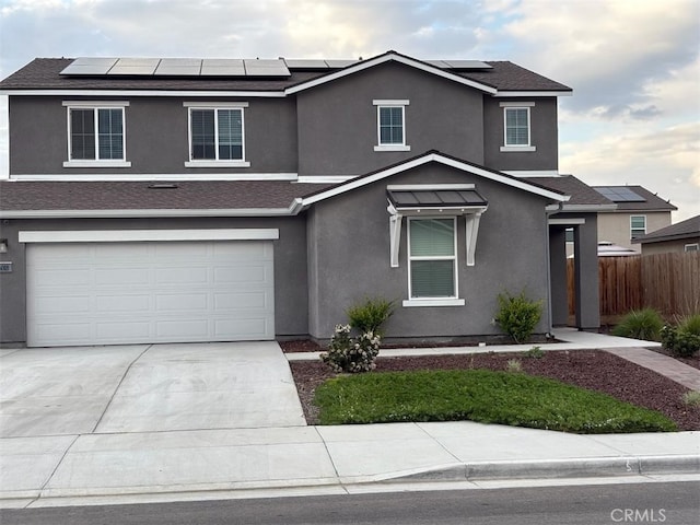 traditional-style house with fence, a garage, stucco siding, roof mounted solar panels, and driveway