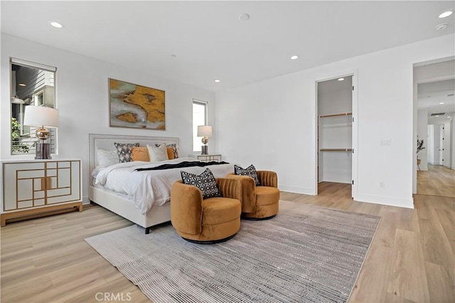 bedroom with baseboards, recessed lighting, light wood-style flooring, and a walk in closet