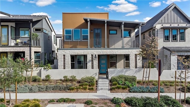 modern home featuring fence, board and batten siding, a balcony, and stone siding