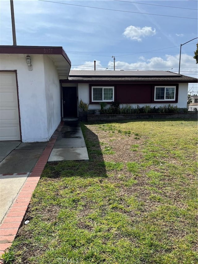 ranch-style house with roof mounted solar panels, stucco siding, and a front yard