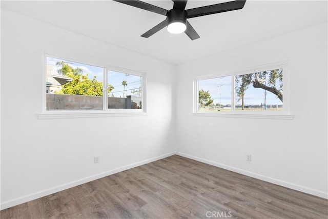 spare room featuring baseboards, a ceiling fan, wood finished floors, and a wealth of natural light
