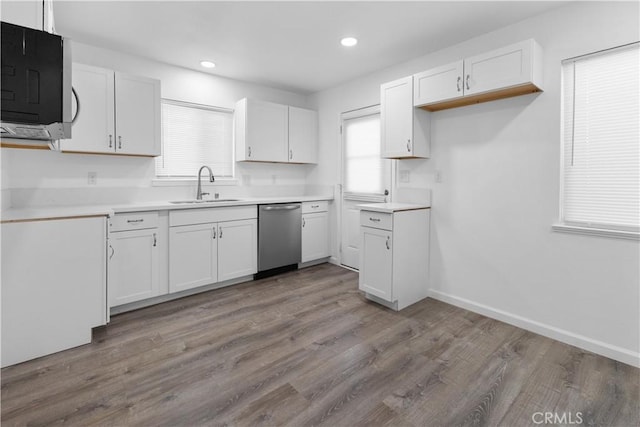 kitchen featuring stainless steel dishwasher, wood finished floors, a sink, recessed lighting, and white cabinetry
