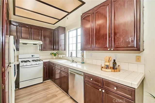 kitchen featuring white appliances, light wood-style floors, under cabinet range hood, a sink, and backsplash