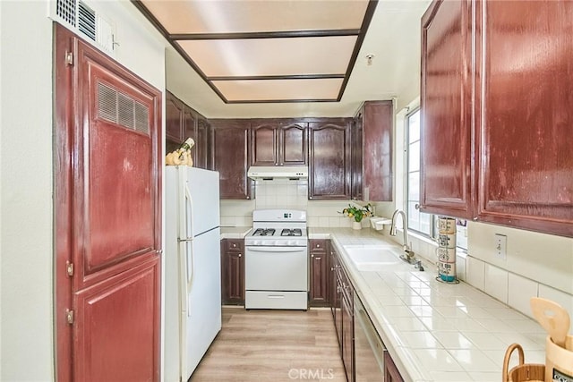 kitchen featuring visible vents, white appliances, tile counters, under cabinet range hood, and a sink