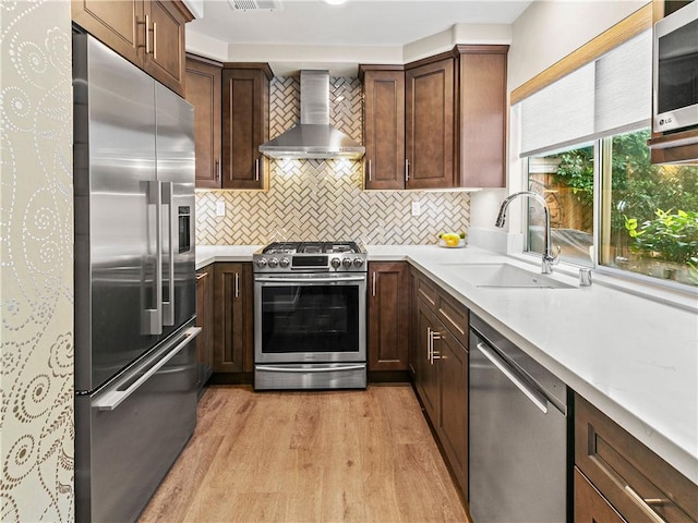 kitchen featuring light countertops, wall chimney exhaust hood, a sink, light wood finished floors, and stainless steel appliances