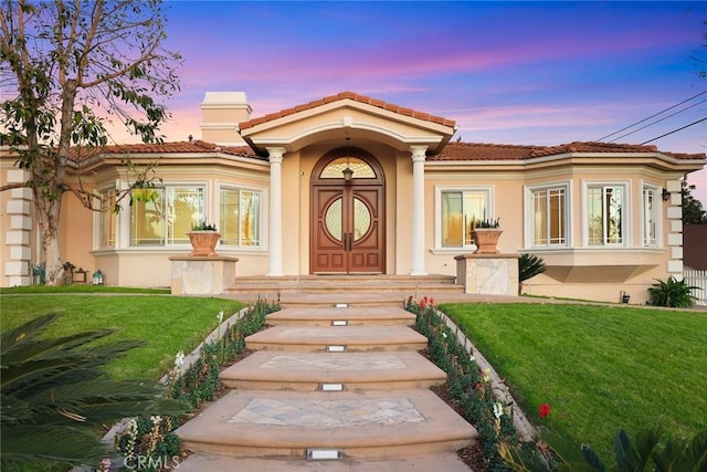 view of front facade with a lawn, stucco siding, and a tiled roof
