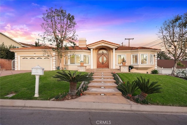 mediterranean / spanish home featuring driveway, a tile roof, a front yard, an attached garage, and stucco siding