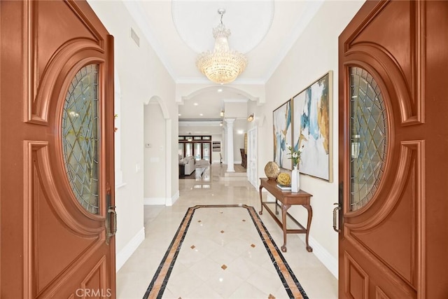 entrance foyer with visible vents, arched walkways, baseboards, decorative columns, and a notable chandelier