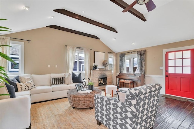 living room with vaulted ceiling with beams, ceiling fan, a stone fireplace, and wood finished floors