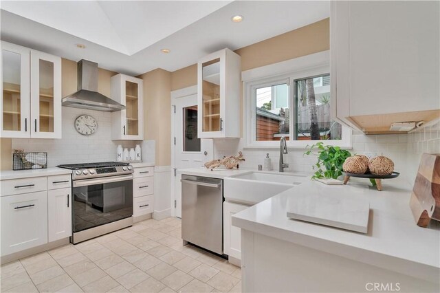kitchen with wall chimney exhaust hood, backsplash, appliances with stainless steel finishes, and light countertops
