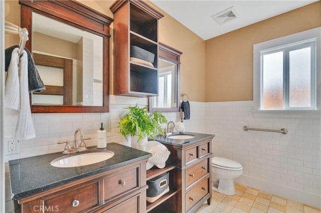 bathroom with tile walls, vanity, toilet, a wainscoted wall, and visible vents