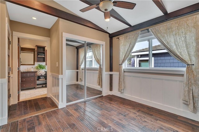 unfurnished bedroom featuring vaulted ceiling with beams, a decorative wall, wainscoting, a closet, and dark wood-style flooring