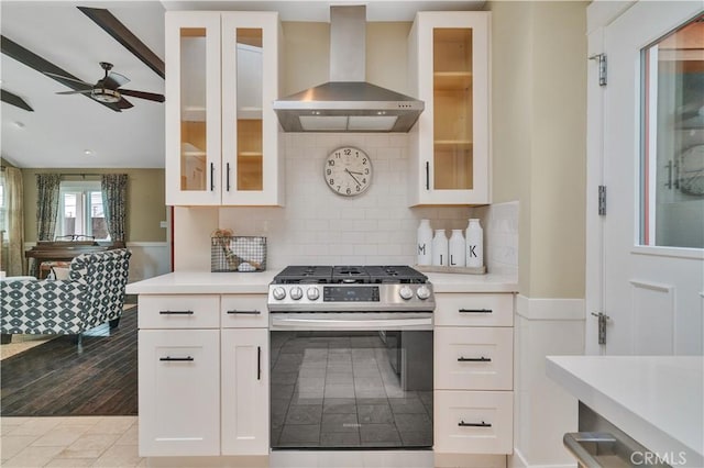 kitchen with wall chimney range hood, stainless steel gas range oven, ceiling fan, and light countertops