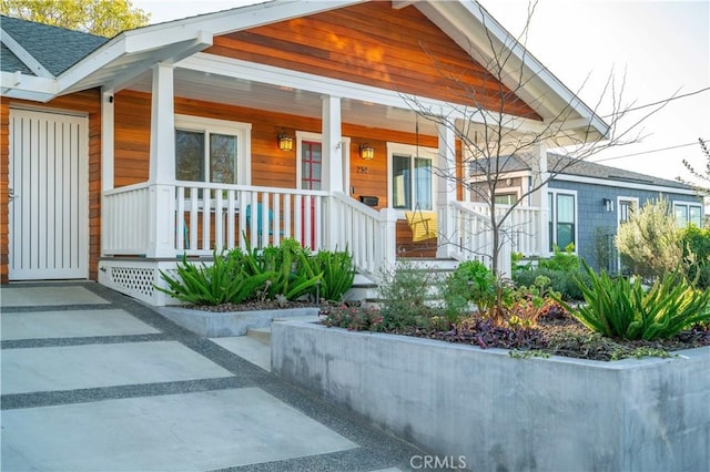 entrance to property featuring covered porch and roof with shingles