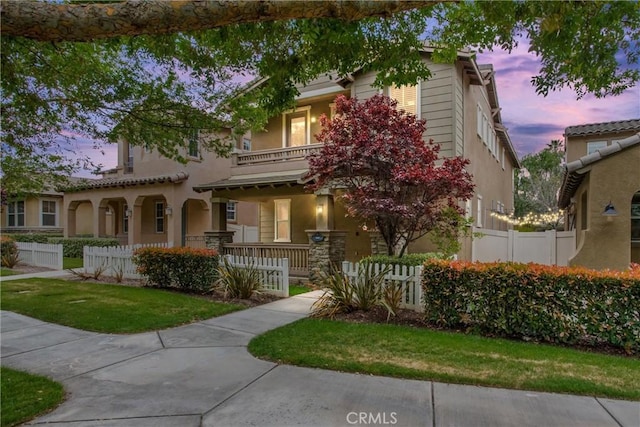 view of front of house with fence private yard, stucco siding, a porch, and a balcony