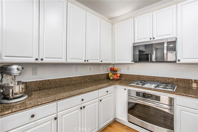kitchen featuring white cabinets, stainless steel appliances, and dark stone countertops