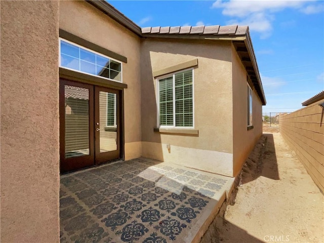 entrance to property featuring fence, french doors, and stucco siding