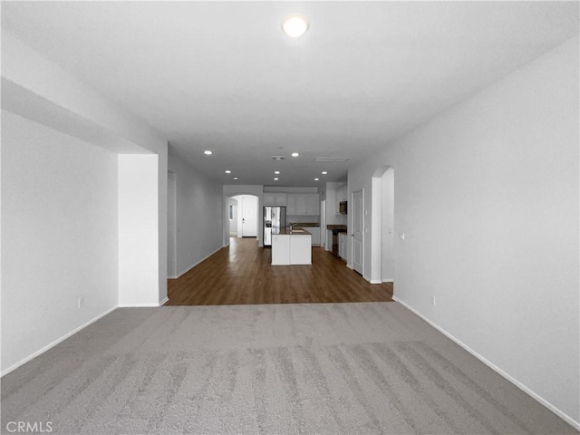 unfurnished living room featuring recessed lighting, arched walkways, baseboards, and dark colored carpet