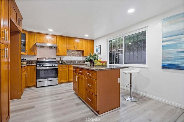 kitchen with gas range, light wood-style floors, a kitchen island, brown cabinets, and baseboards