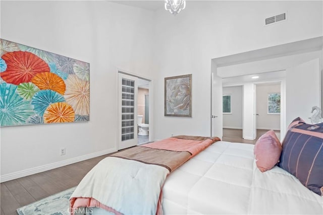 bedroom with a high ceiling, visible vents, wood finished floors, and baseboards