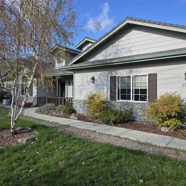 view of front of property featuring covered porch, a front lawn, and stone siding
