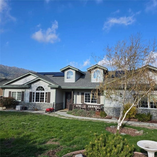 view of front of house with covered porch, stone siding, solar panels, roof with shingles, and a front lawn