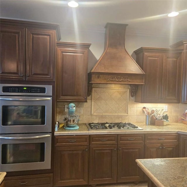 kitchen featuring tasteful backsplash, stainless steel appliances, custom range hood, and light countertops