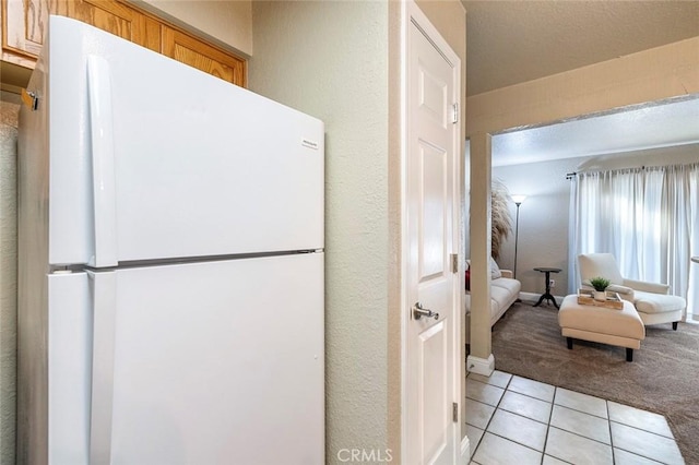 kitchen with light tile patterned floors, freestanding refrigerator, and light carpet